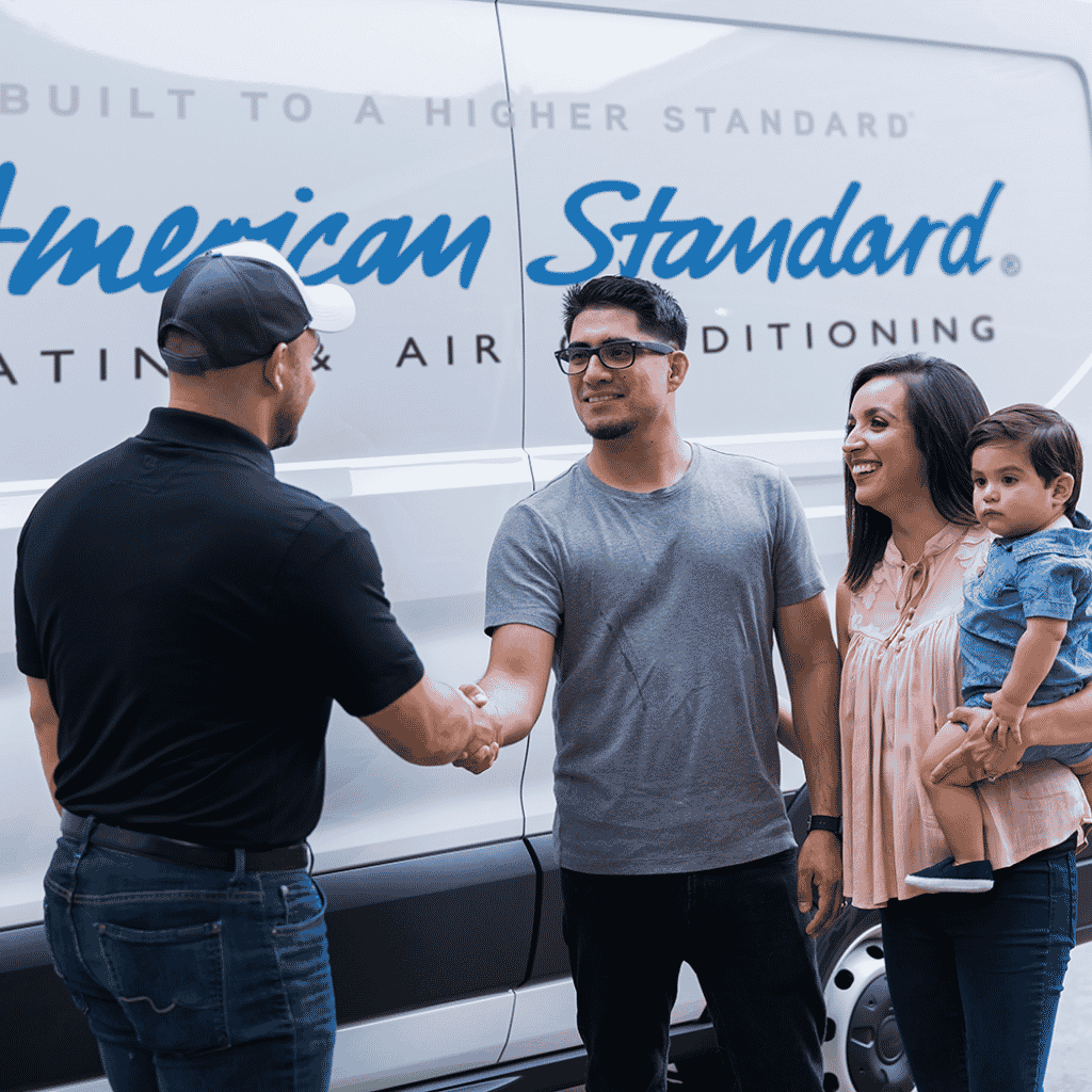 Technician shaking hands with a family in front of an American Standard service van