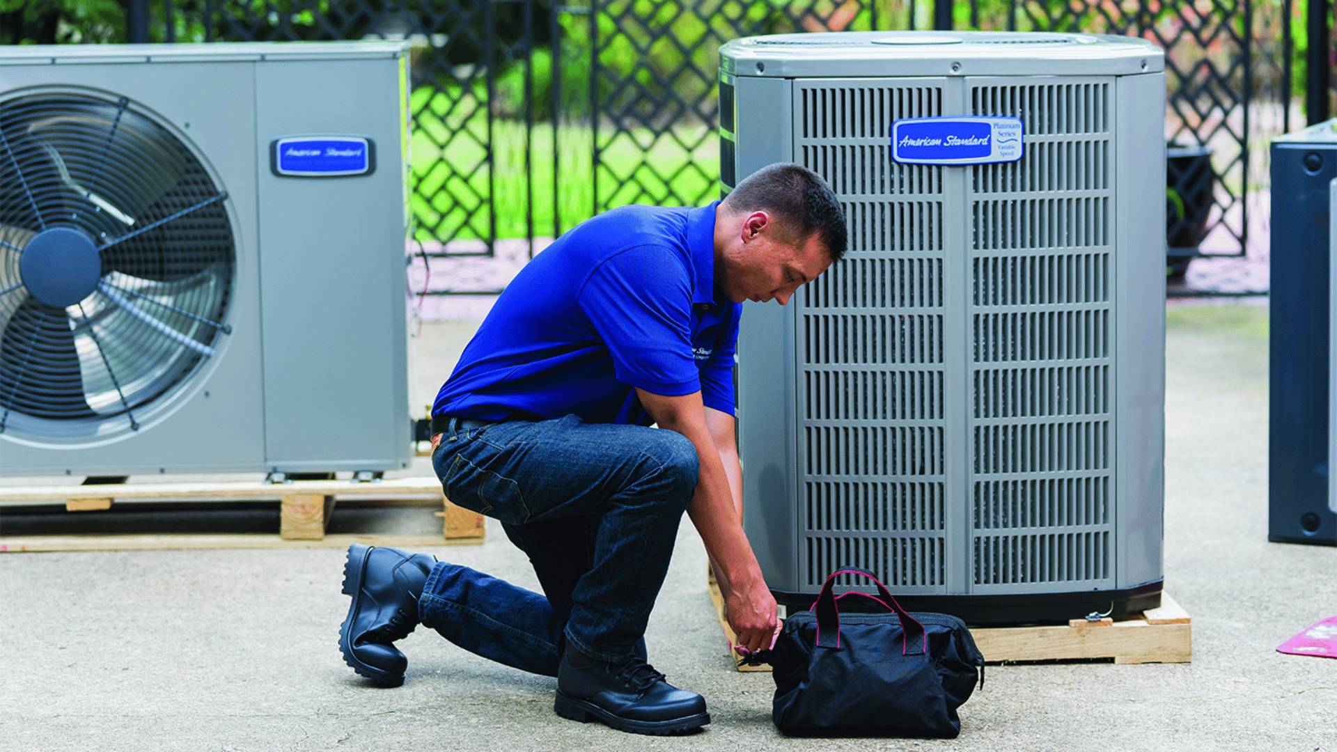 Technician kneeling beside a tool bag next to two outdoor air conditioning units