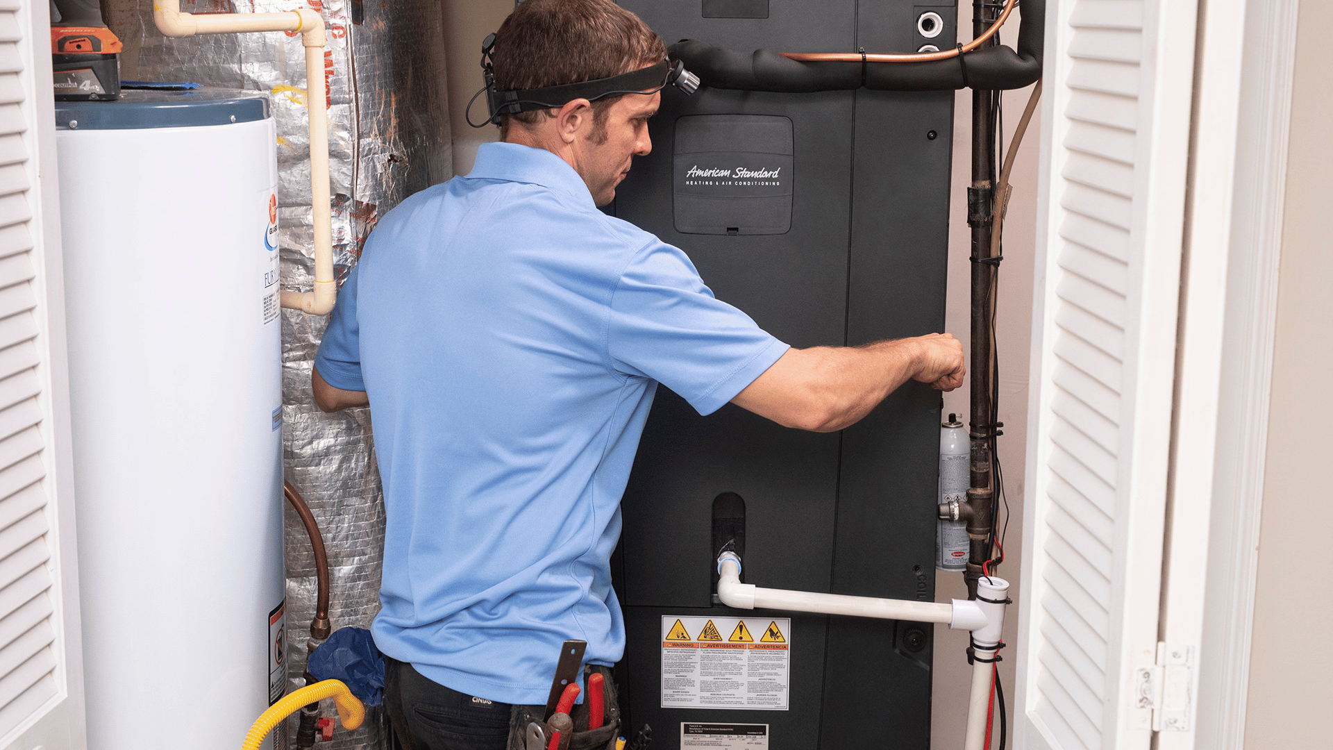 Technician working on a furnace unit next to a water heater in a home utility closet