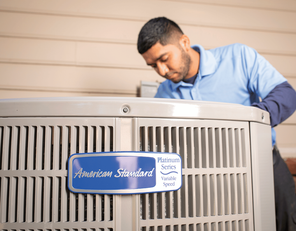 Technician inspecting an American Standard air conditioning condenser unit
