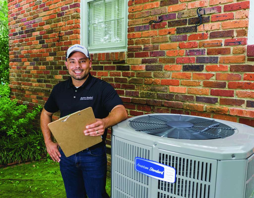 Smiling technician holding a clipboard beside an outdoor heat pump unit