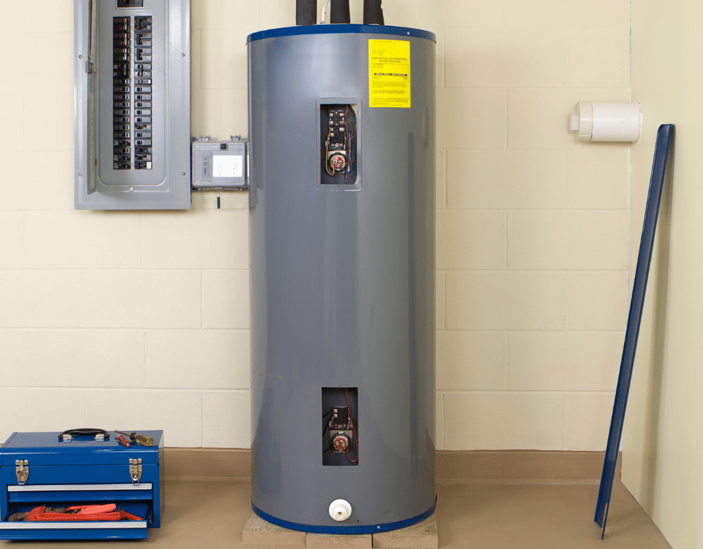 Gray tank water heater installed beside an electrical panel with a technician's tool box nearby
